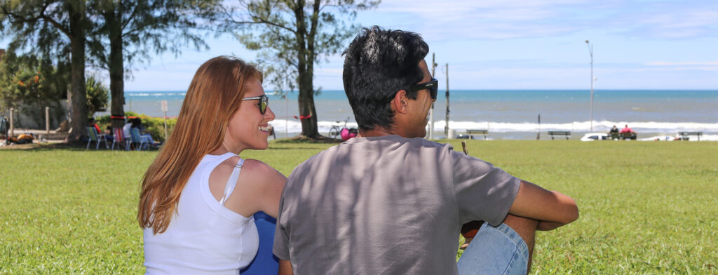 Um homem e uma mulher sentados na grama, olhando para o mar, em um dia ensolarado em Torres.