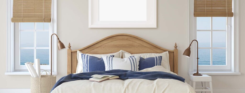 Uma cama com aspectos rústicos encostada em uma parede branca com janelas que mostram o mar.